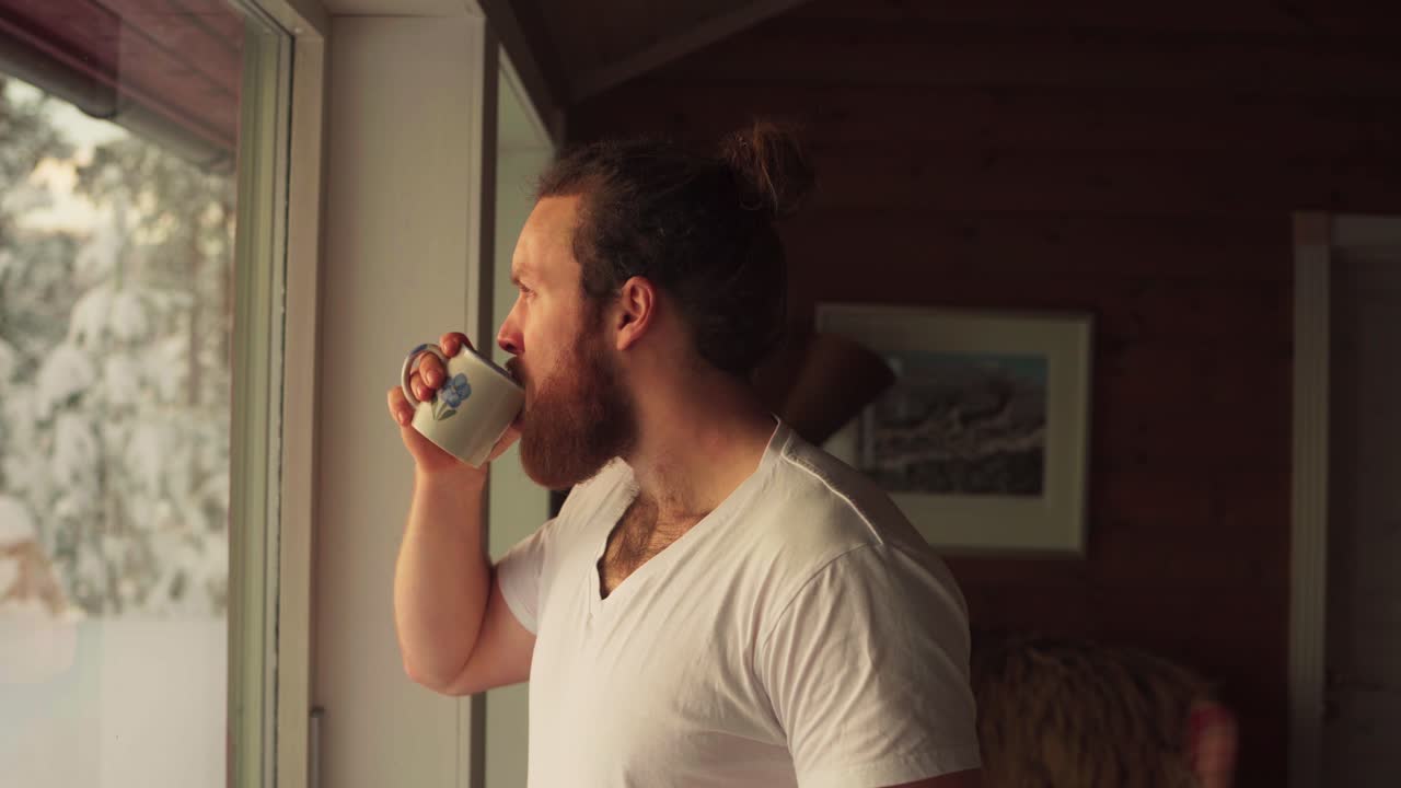 겨울에 창가에 서서 아침에 뜨거운 커피를 마시는 집에서 유럽 남자