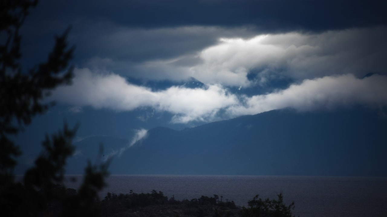 Dramatic white clouds moving over a mountain range above the ocean