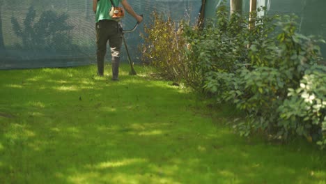 unrecognizable man trimming green grass with brush cutter electric