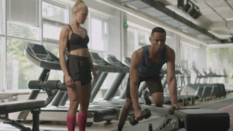 Vista-Frontal-De-Una-Monitora-Caucásica-Y-Un-Atlético-Afroamericano-En-El-Gimnasio.