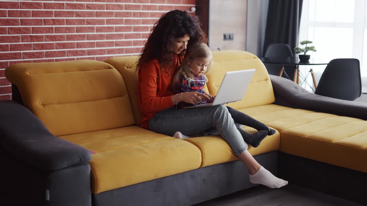 Mother and daughter sitting on the couch and typing on laptop