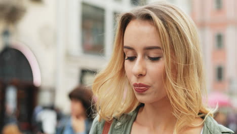 Close-up-view-of-Caucasian-blonde-woman-texting-on-the-smartphone-while-walking-down-the-street-and-drinking-coffee-to-go