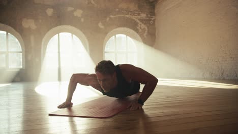 a male athlete in a black sports uniform uses a unique push-up technique and swaying from one side to the other for a more intense pumping of his muscles in a sunny brick gym