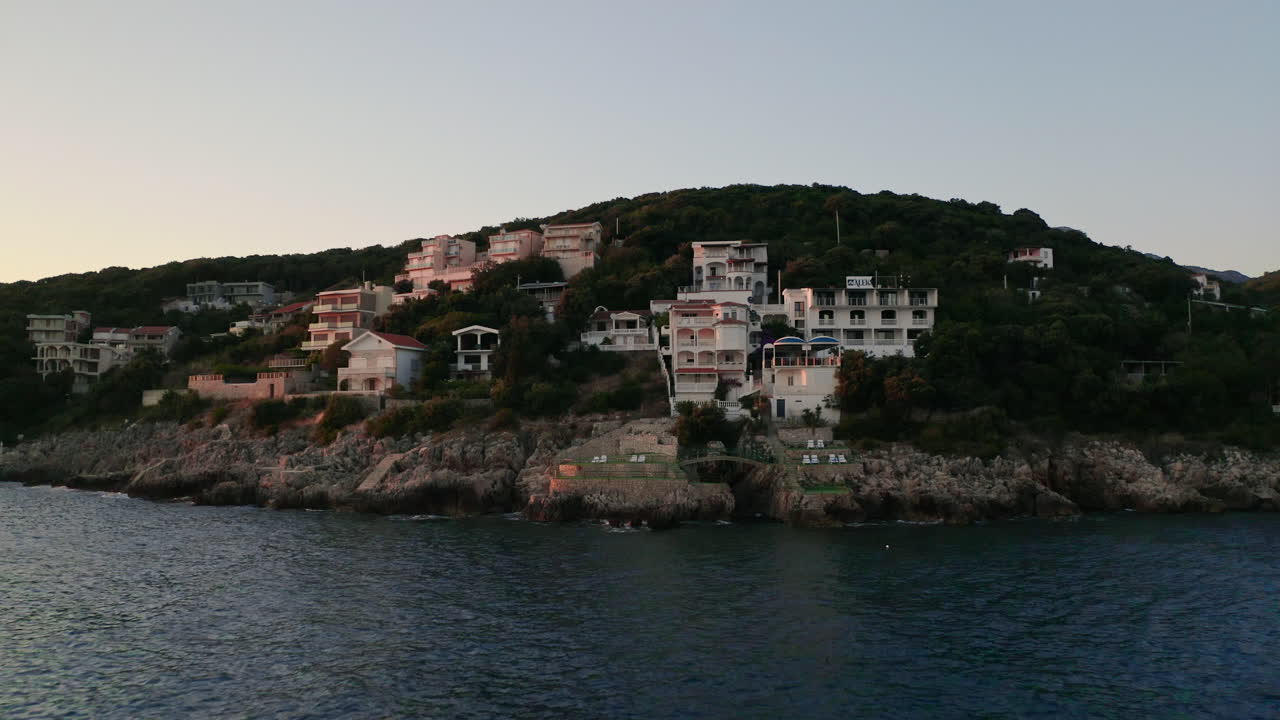 아드리아 해안의 몬테네그로 우체하(utjeha) 해안 마을, 바다 위의 바위 절벽에 서 있는 고급 빌라, 뒤에 있는 큰 산, 해변 가까이에 정박된 높은 돛대가 있는 요트, 공중