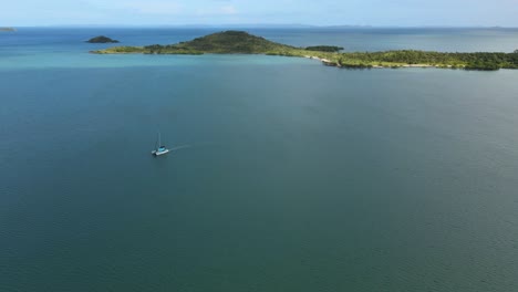 clip aéreo de un catamarán en el océano tranquilo, islas tropicales y sol detrás