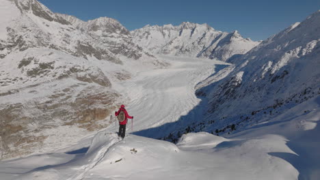 Toma-Aérea-En-Suiza-Con-Una-Persona-Caminando-Con-Raquetas-De-Nieve-En-Un-Día-Soleado-Con-Un-Glaciar-Detrás