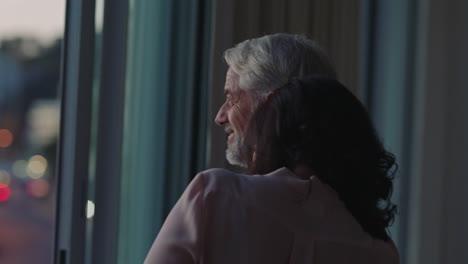 happy couple hugging at home looking out window at sunset enjoying successful retirement lifestyle on vacation sharing romantic connection