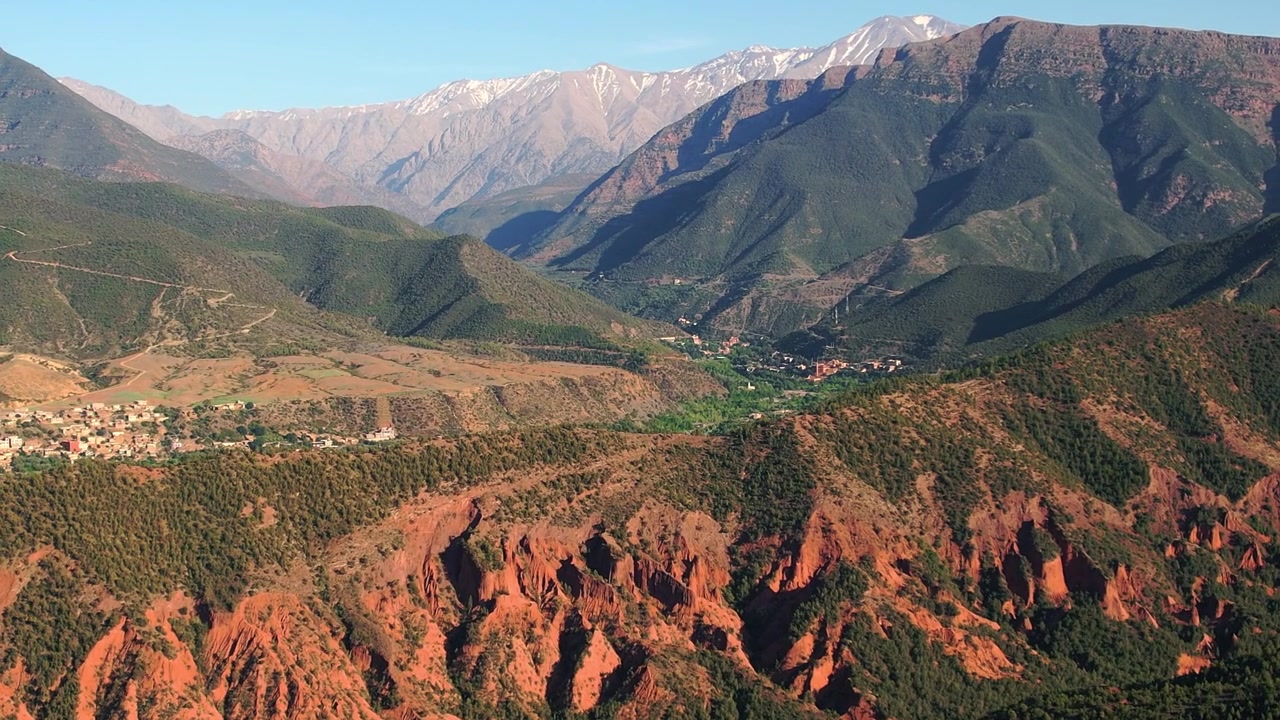 Ourika Vadisi, Al Haouz Eyaleti, Marakeş Safi, Fas'ta kırmızı tortul yamaçlar, ardıç ormanlığı, Berberi köyleri, sulanan vadi tabanları ve Yüksek Atlas Dağları'nı içeren drone yörünge çekimi.