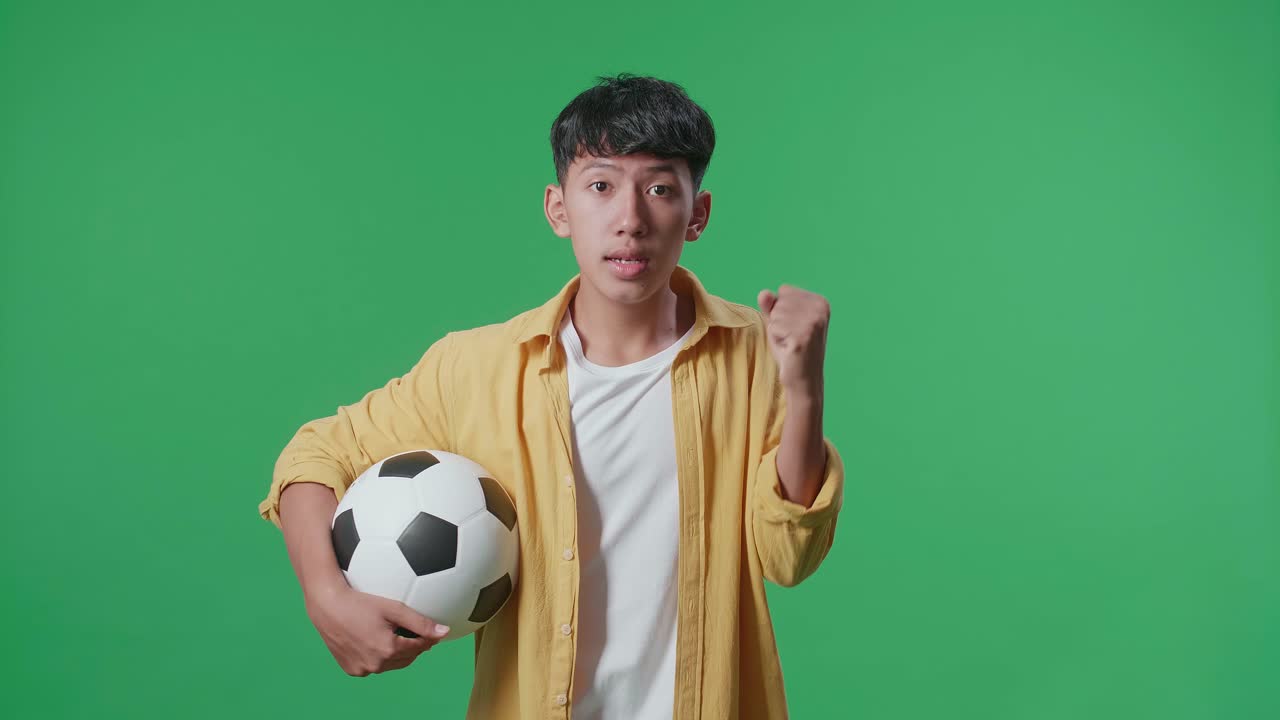 흥분 된 아시아 소년 은 공 을 들고 골 을 기 위해 응원 하고 있으며, 초록색 스크린 배경 에서 축구 를 응원 하고 있다