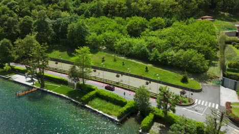 Red-car-driving-on-panoramic-road-along-Orta-Lake,-Pella-town-in-Italy