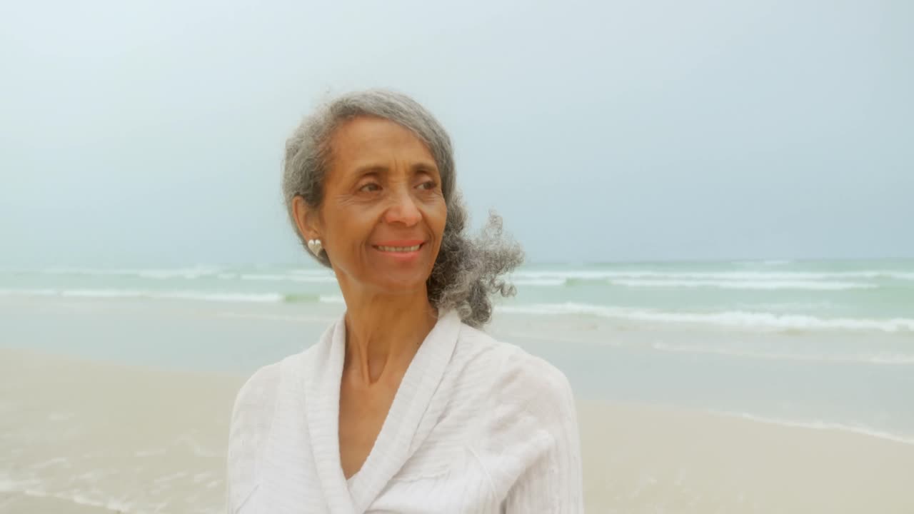 Front view of thoughtful active senior African American woman standing on the beach 4k