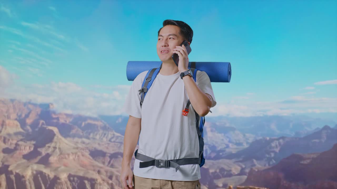 Asian Male Hiker With Mountaineering Backpack Smiling And Talking On Smartphone While Traveling At The Top Of Mountain