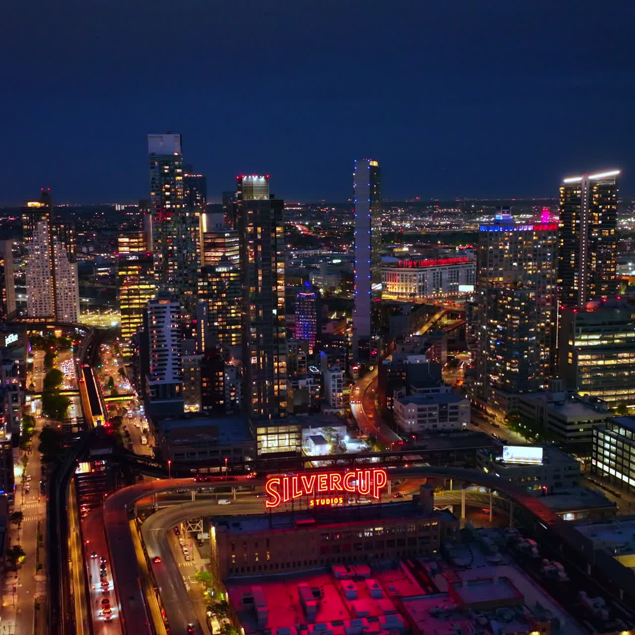 Building of Silvercup Studios neighboring amazing modern architecture. Lights of New York city at night aerial view