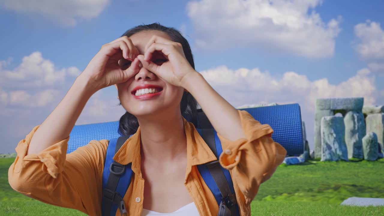 Close Up Of Asian Female Hiker With Mountaineering Backpack Smiling And Making Binoculars Gesture Then Looking Around While Traveling In Stonehenge