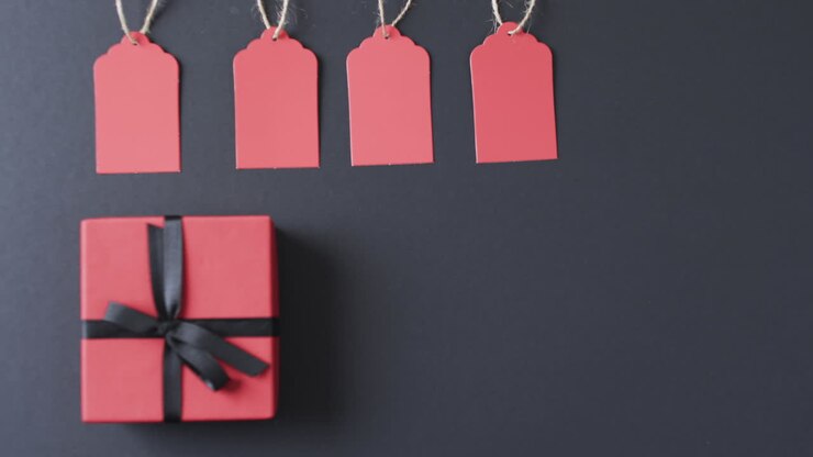 Video of gift tags on string, red gift box with ribbon and copy space on black background