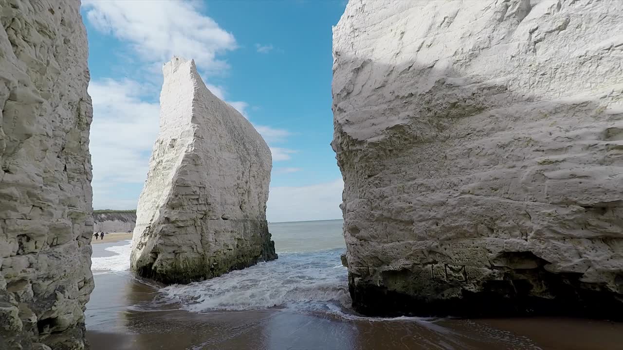 Scenic view of Botany Bay in Broadstairs, Kent, England, featuring dramatic white chalk cliffs, clear blue sky, and gentle sea waves washing the sandy shoreline along the coast