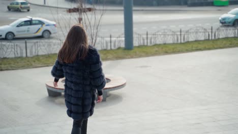 girl in winter coat in the city. beautiful woman in luxury fur coat posing on camera in the city park. glamour model in the street. slow motion.