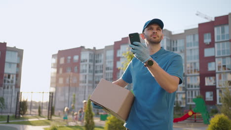 Un-Mensajero-Masculino-Está-Buscando-Un-Teléfono-Móvil-Para-Entregar-La-Dirección-De-Comida-De-Una-Tienda.-El-Repartidor-Navega-Por-Teléfono-En-La-Ciudad-Buscando-Direcciones-De-Entrega-De-Tiendas.-Entrega-Rápida