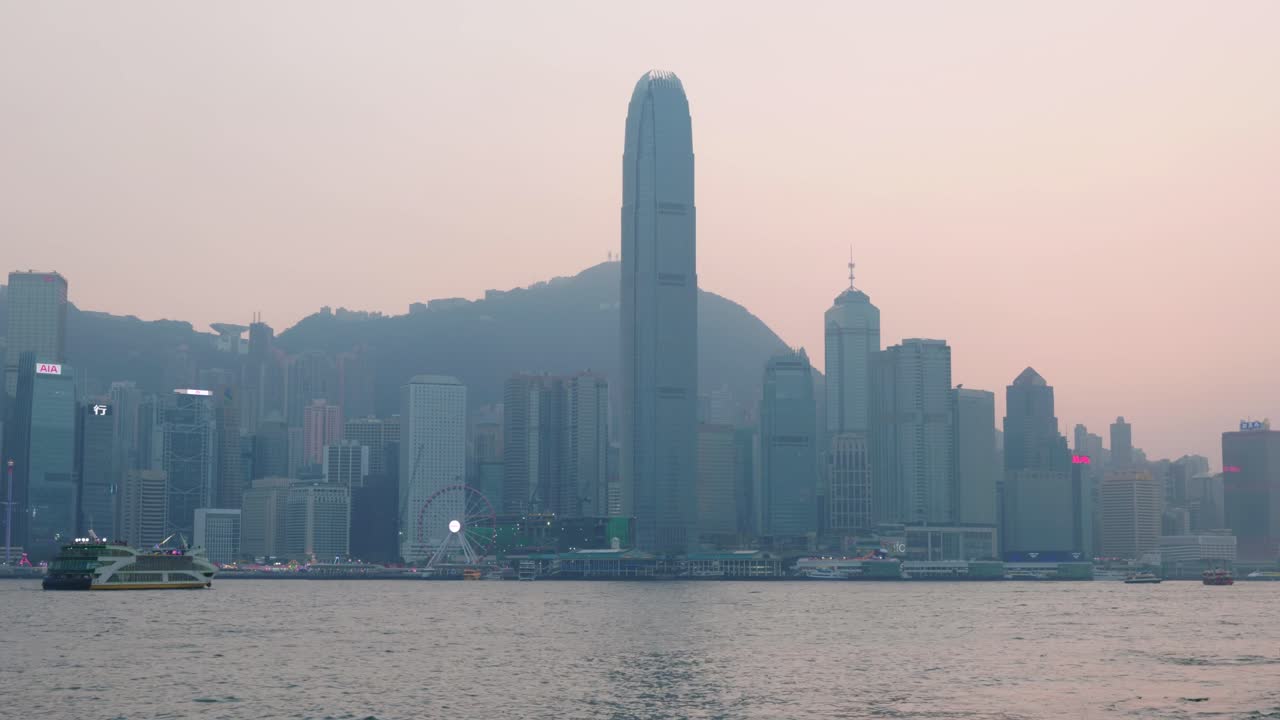 Vista panorâmica do arranha-céu Two International Finance Center a partir do Victoria Harbour no centro de Hong Kong durante o pôr do sol, apresentando luz quente sobre a icônica linha do horizonte.
