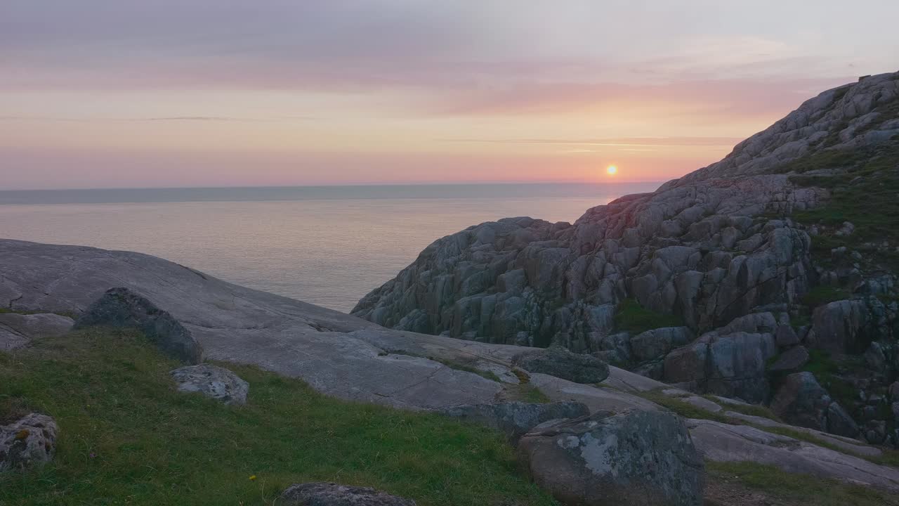 viendo desde la cima de un acantilado a lo largo de la costa hasta el horizonte, con vistas al océano tranquilo con una hermosa puesta de sol rosada y un cielo despejado