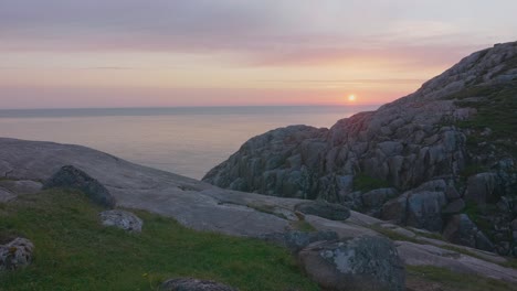 Viewing-from-the-top-of-a-cliff-along-the-coastline-out-to-the-horizon,-overlooking-the-calm-ocean-with-a-beautifully-rich-pink-sunset-and-clear-sky