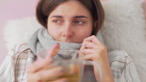 sick girl lying in bed coughing and sniffing, girl drinks tea wrapped in scarf