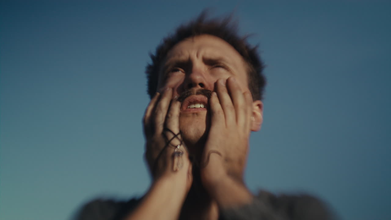 Man with hands on face looking up at the sky