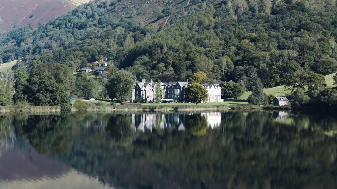 Aerial orbit around grand lakeside hotel reflecting in Grasmere’s still water, England