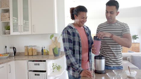 Happy-diverse-gay-male-couple-preparing-healthy-fruit-smoothie-in-kitchen,-copy-space,-slow-motion