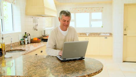 hombre maduro usando una computadora portátil en la cocina