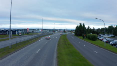 Vorwärtsflug-über-Breite-Mehrspurige-Bundesstraße-Mit-Kreuzung.-Autos-Halten-An-Ampeln.-Grüne-Rasenfläche-Entlang-Der-Straße.-Reykjavik,-Island