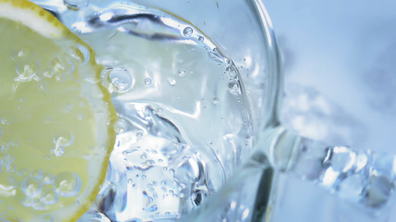 Slow Motion - Close shot of a tasty lemon slice dropping into a cold and refreshing glass of sparkling water