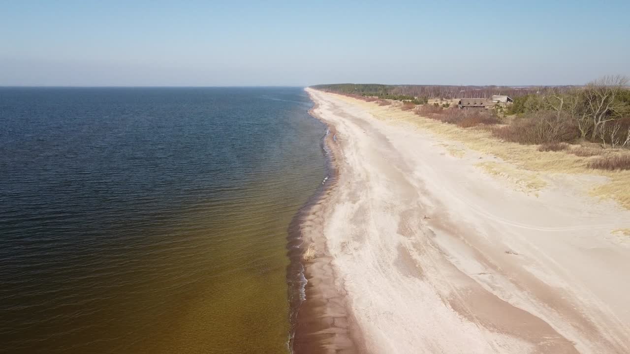 vista aérea de las olas del mar rompiendo en la playa con arena blanca en un soleado día de primavera, mar báltico, playa de pape, letonia, gran angular que revela el disparo de un dron que se mueve hacia atrás, la cámara se inclina hacia arriba