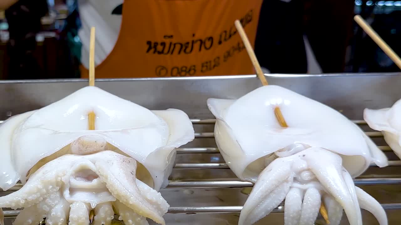 Close-up of squid and skewered meats being grilled at a vibrant market stall.