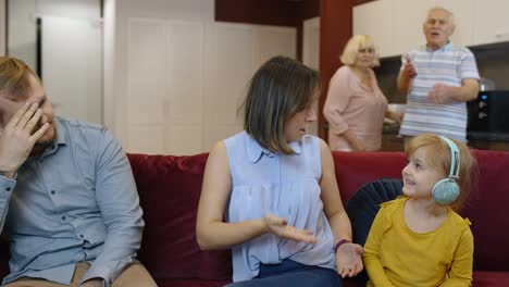 una familia está sentada en el sofá y hablando. la chica de la camisa amarilla está escuchando música en los auriculares y sonriendo. los abuelos están en el fondo.