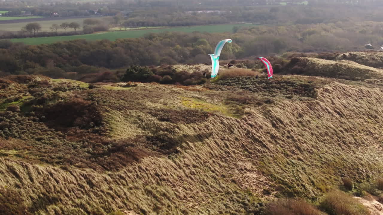 Top view of three Dutch paragliders soaring along vegetated coastal dune