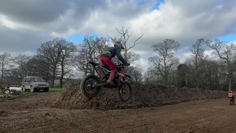 slow motion video of a young professional motocross rider jumping at the peak of a large and steep hill in the countryside of england whilst competing in a competition