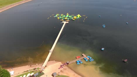 Gente-Divirtiéndose-En-Un-Parque-Acuático-Inflable-En-El-Lago-Del-Depósito-De-Agua-Bewl-Durante-El-Día-Soleado-En-Kent,-Reino-Unido