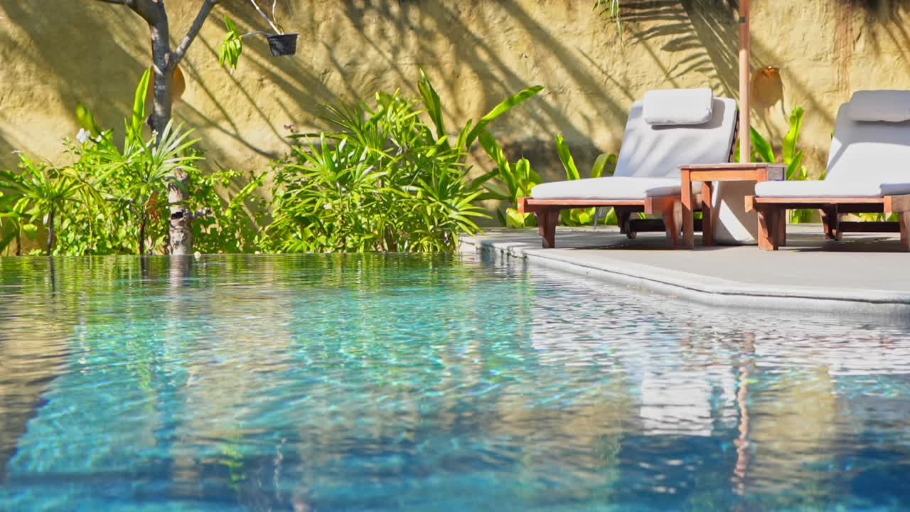 Zwei leere Strandliegen am Rand eines Resort-Schwimmbades