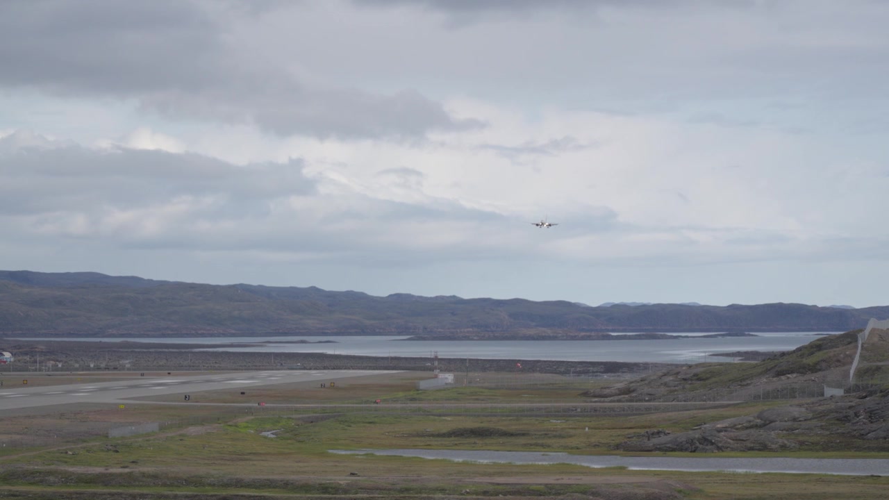 Bredt landskabsbillede af et canadisk North kommercielt passagerfly på sidste indflyvning, lavt over tundra-terrænet og bugten mod landingsbanen