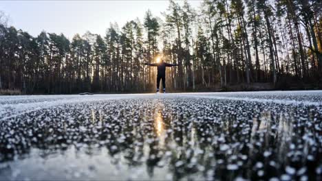 low angle shot of skater in black gliding across glowing icy lake at sunrise