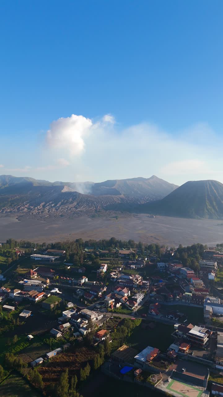 High-altitude drone of Cemoro Lawang village with Mount Bromo and Semeru volcano behind, vertical establish