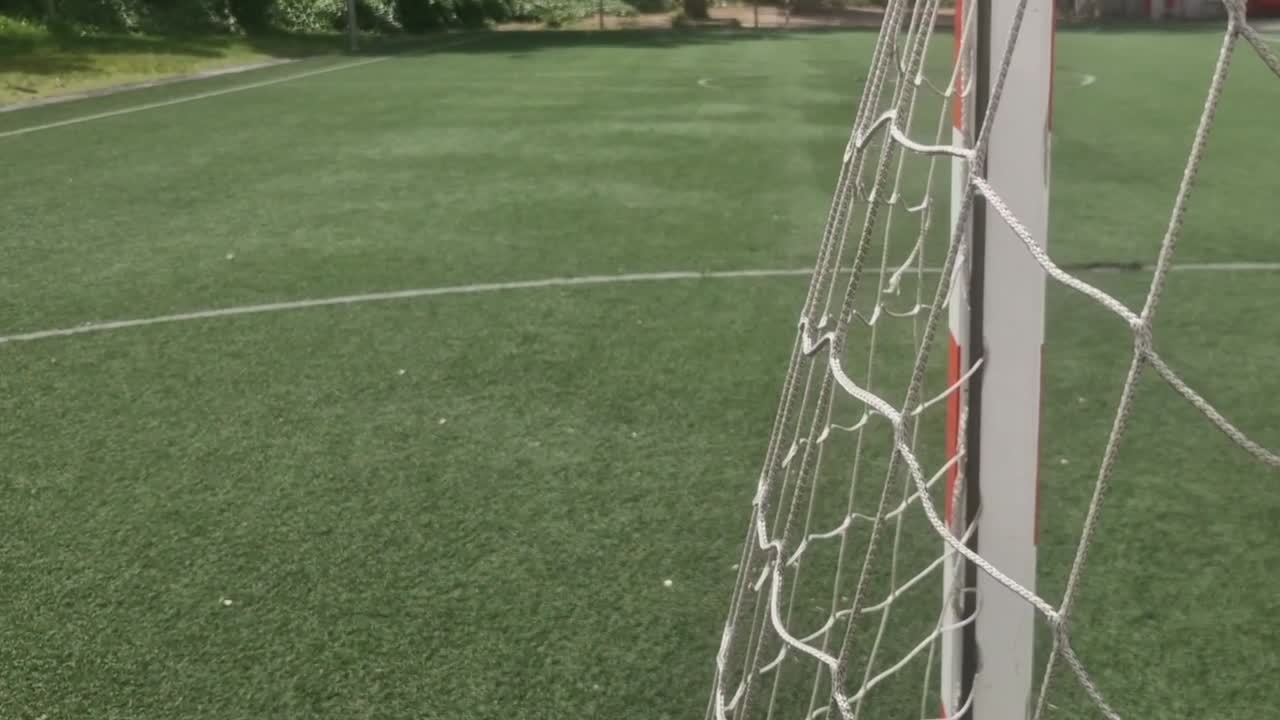 Moving camera shot from inside a football goal looking out onto the empty green artificial field