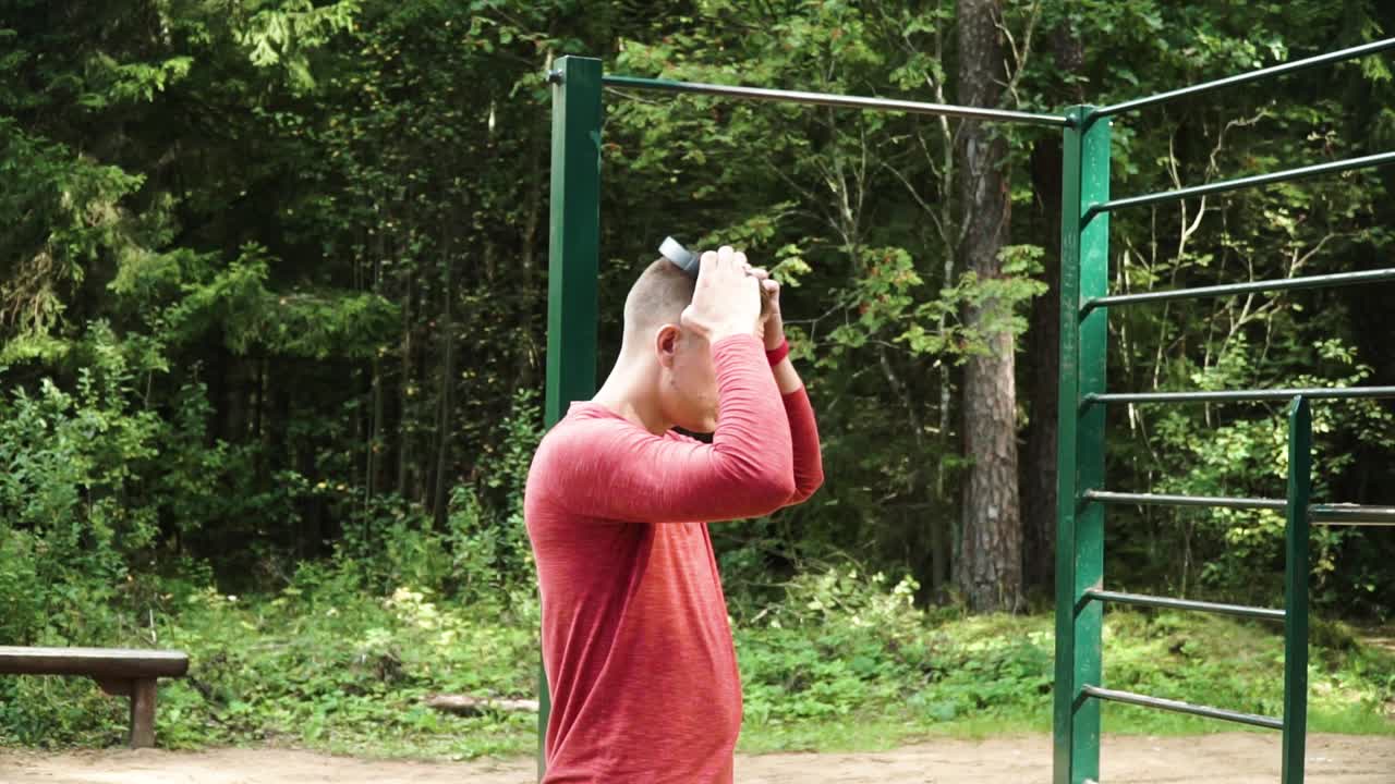 Young male putting headphones to start a workout in the forest next to outdoor fitness, steady profile shot