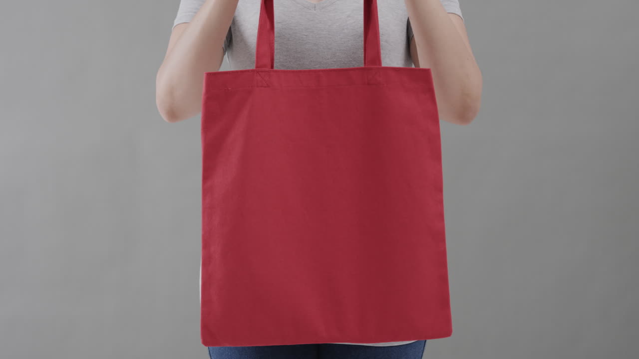 ⁇ 색 티셔츠를 입은 백인 여성이 회색 배경에 빨간 가방을 들고, 복사 공간, 슬로우 모션