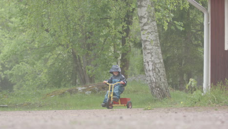 slow motion - a cute child rides a colourful trike in the rain