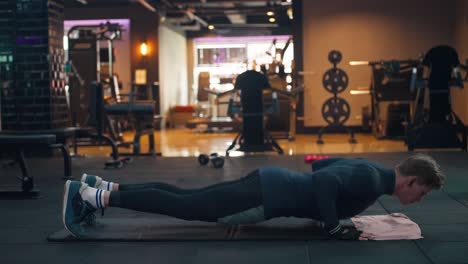 Muscular man doing push ups in the gym. Side view of an athletic caucasian young man in sportswear working out in dim lit gym