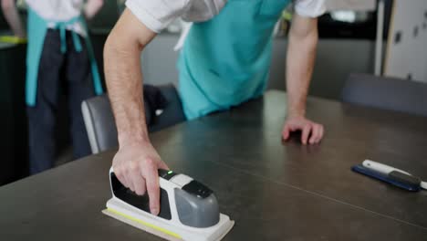 Close-up-of-a-confident-brunette-man-in-a-blue-apron-professional-cleaner-together-with-his-colleague-starting-a-glossy-surface-in-a-modern-kitchen-on-call-from-a-cleaning-company-in-a-modern-apartment