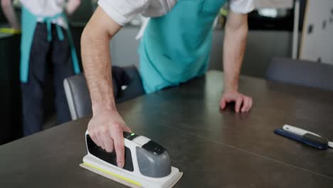 primer plano de un hombre moreno confiado en un delantal azul limpiador profesional junto con su colega comenzando una superficie brillante en una cocina moderna en llamada de una compañía de limpieza en un apartamento moderno