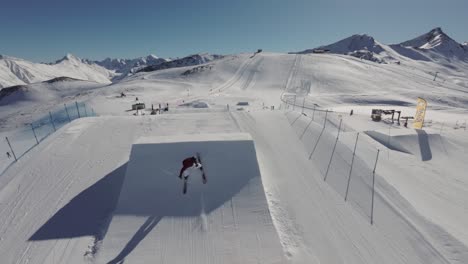 FPV-Luftaufnahme-Eines-Freestyle-Skifahrers,-Der-An-Einem-Sonnigen-Wintertag-Drehungen-Und-Flips-Von-Kickern-Im-Snowpark-Macht,-50-Fps